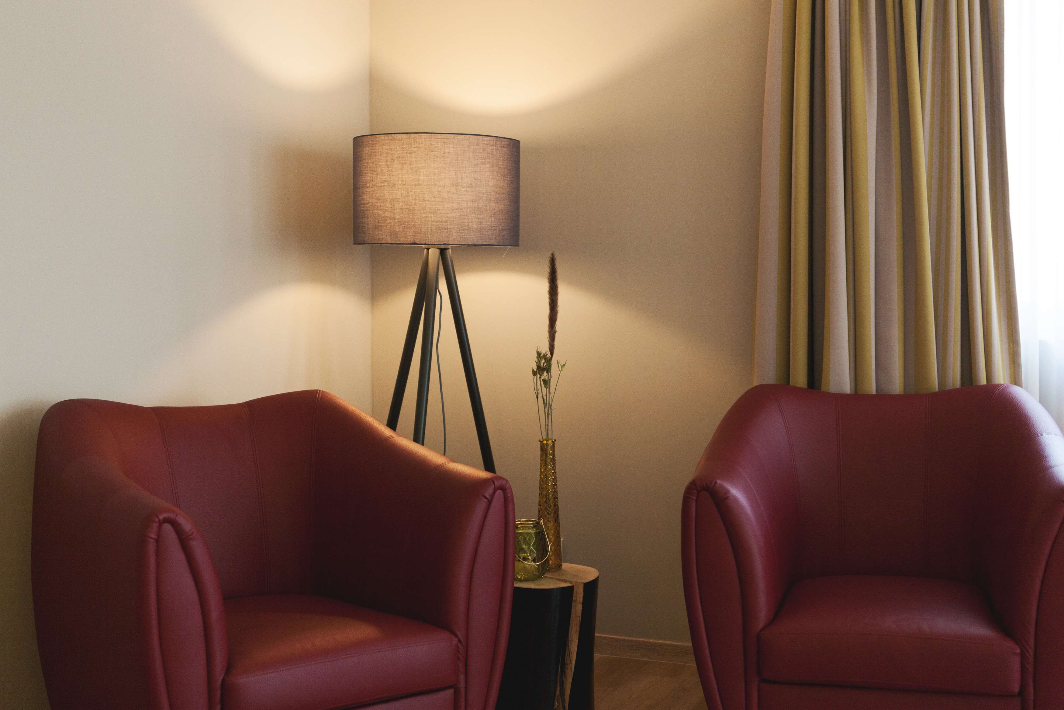 Una habitación con dos sillones de cuero rojo, una lámpara de pie y una mesita con un florero y un objeto decorativo.