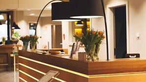 Un mostrador de recepción con detalles de madera iluminados, una lámpara negra y un florero con flores.