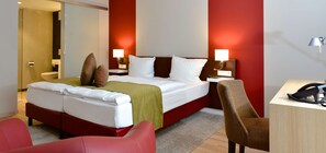Habitación de hotel con cama, dos mesitas de noche con lámparas, un escritorio con teléfono y una silla roja.