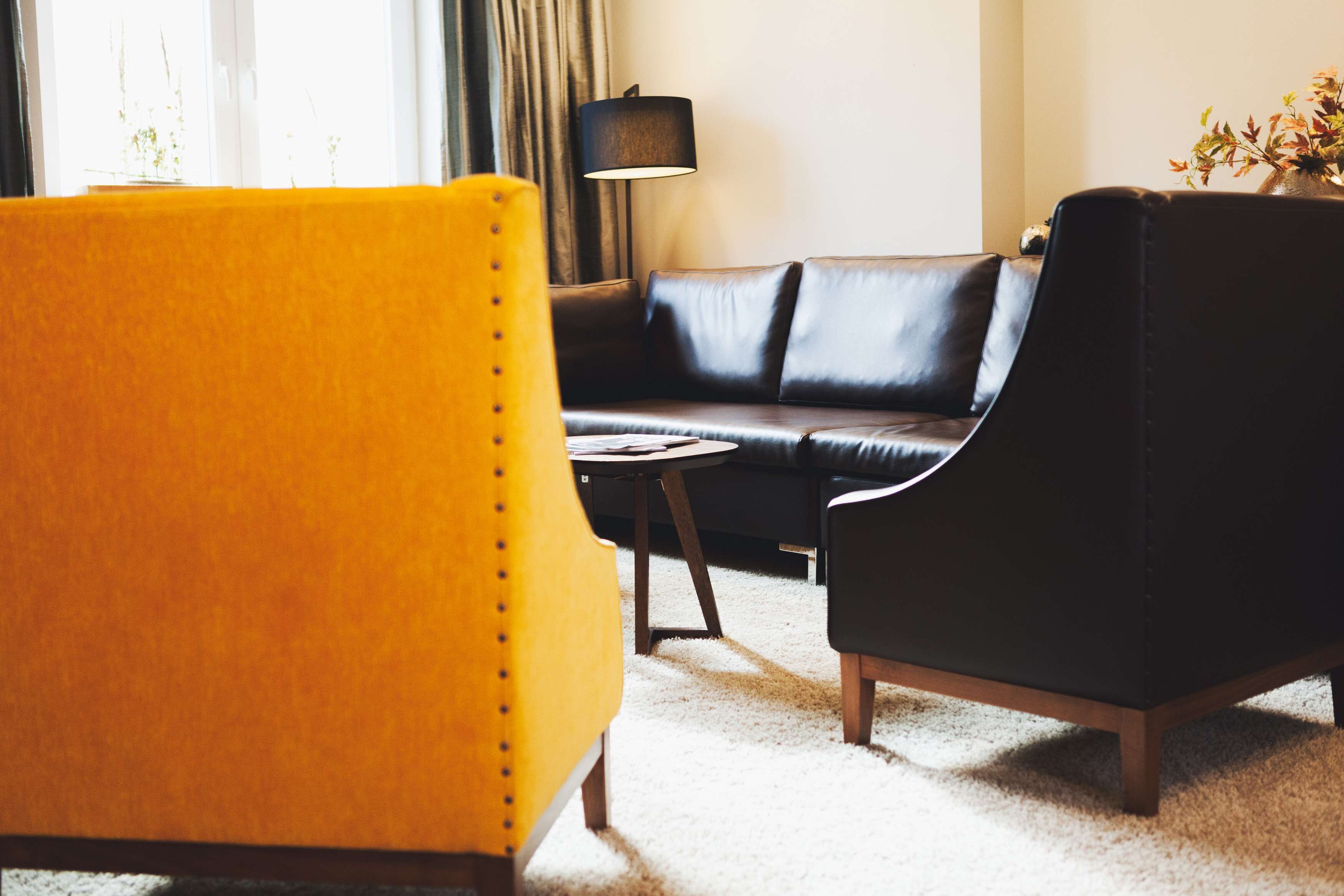 A modern living room with a black leather sofa, a yellow armchair, and a small round table.