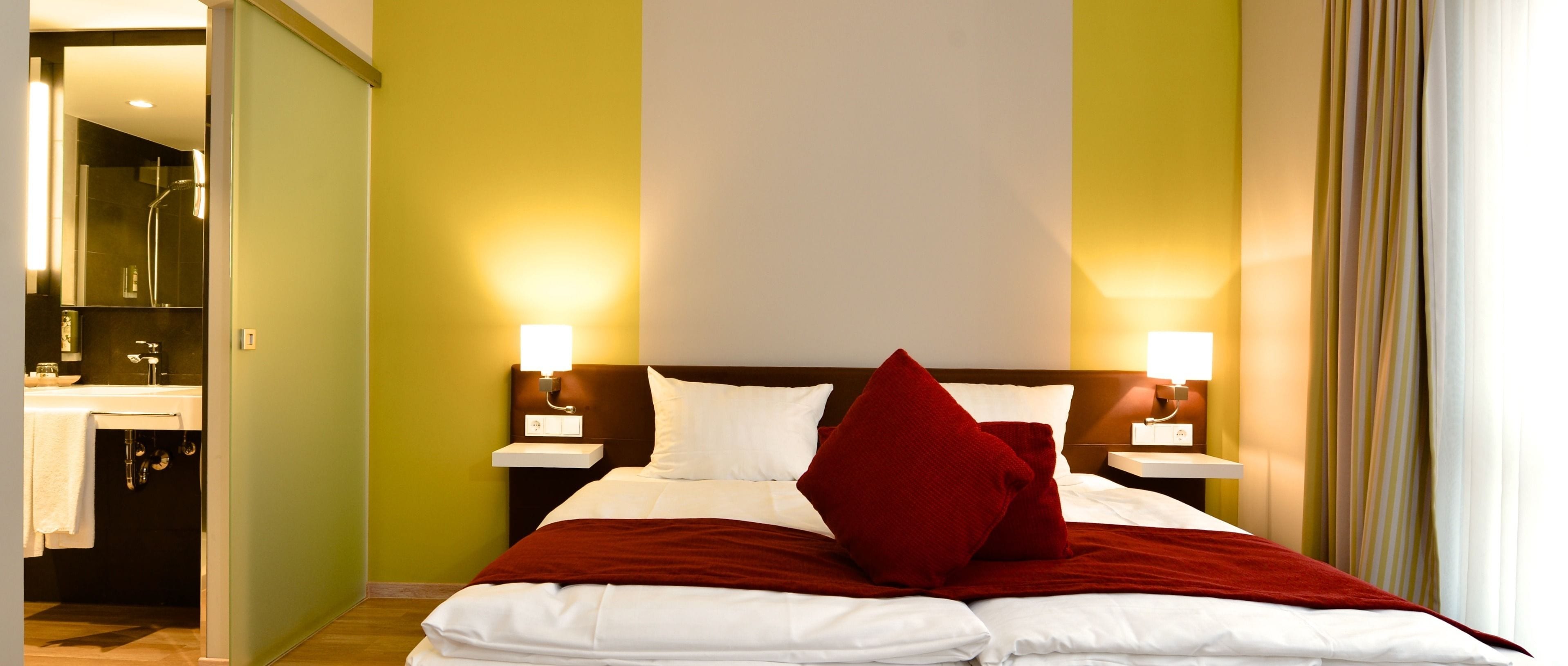 Una habitación de hotel con cama, dos mesitas de noche y un baño con lavabo y ducha.