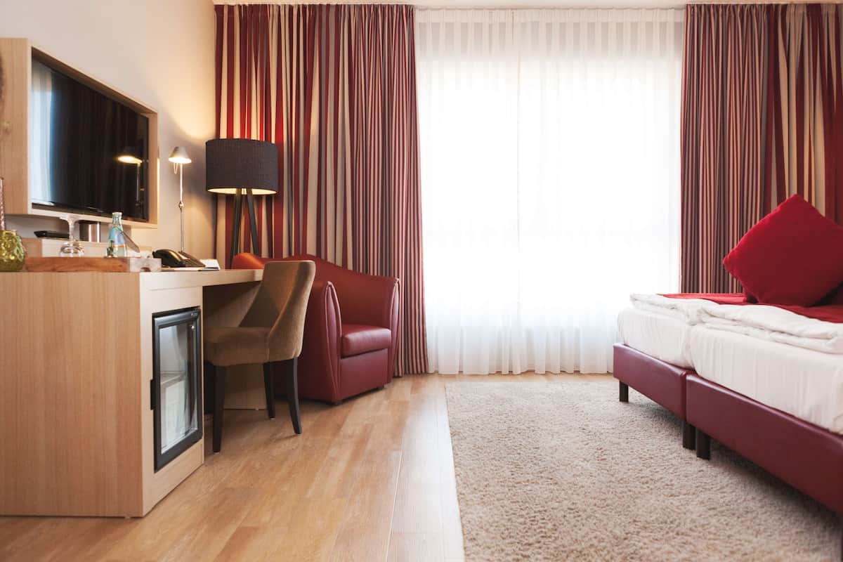 Habitación de hotel con escritorio de madera, una silla, cama con almohadas rojas, televisor y cortinas a rayas.