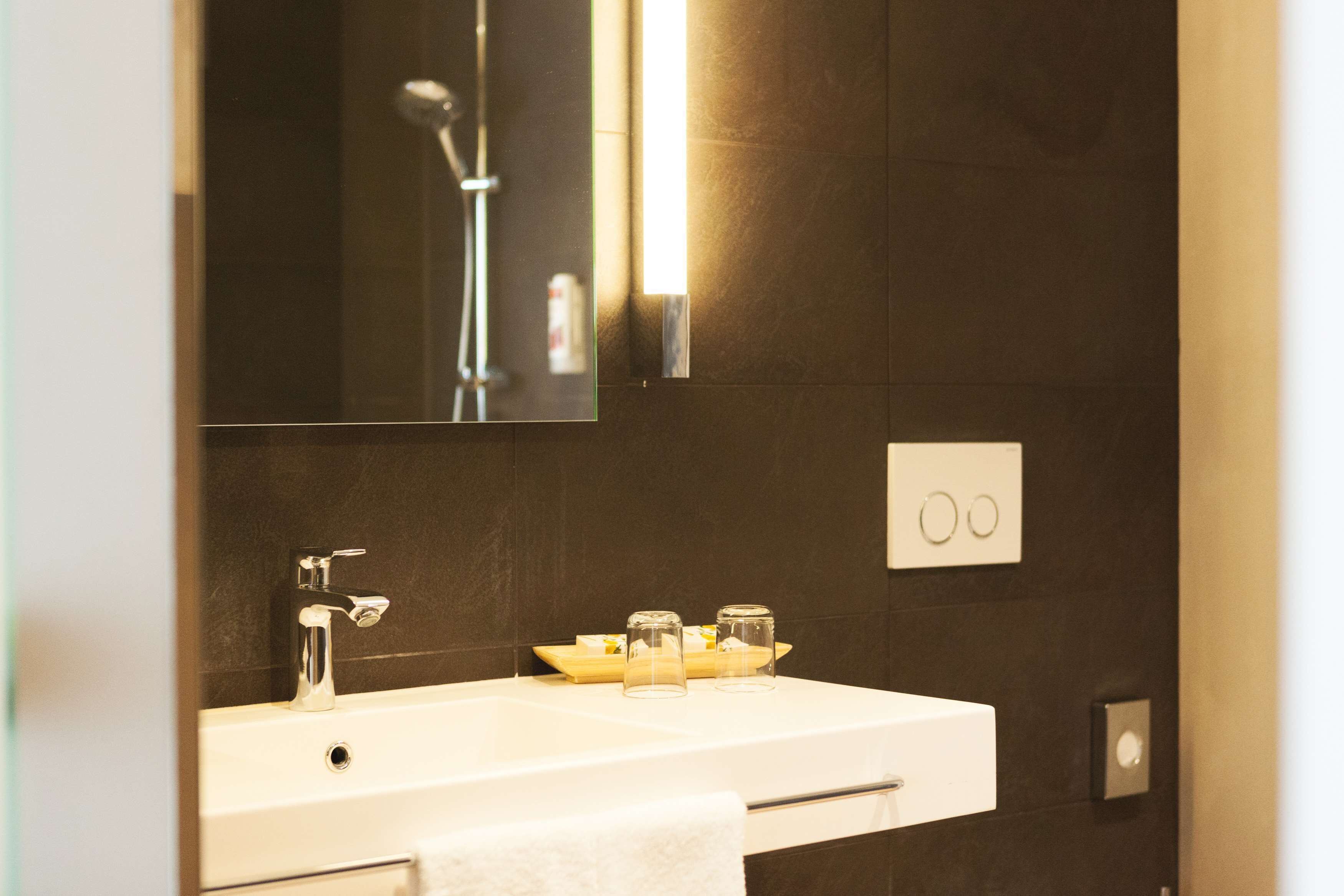 A bathroom with a white sink, a mirror, a showerhead, and a towel hanging on the wall.
