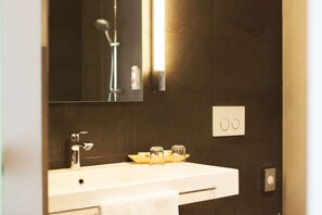 Un baño con un lavamanos blanco, un espejo, un cabezal de ducha y una toalla colgada en la pared.