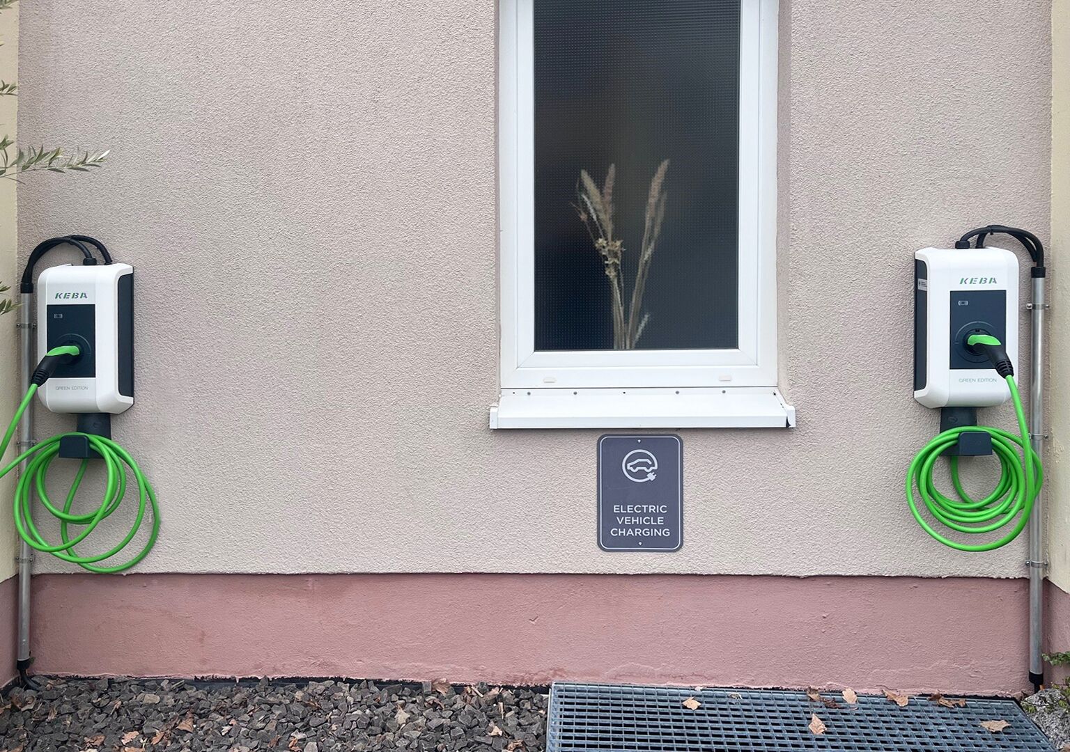 An electric vehicle charging station with two KEBA chargers, a charging sign, and a window with a plant.