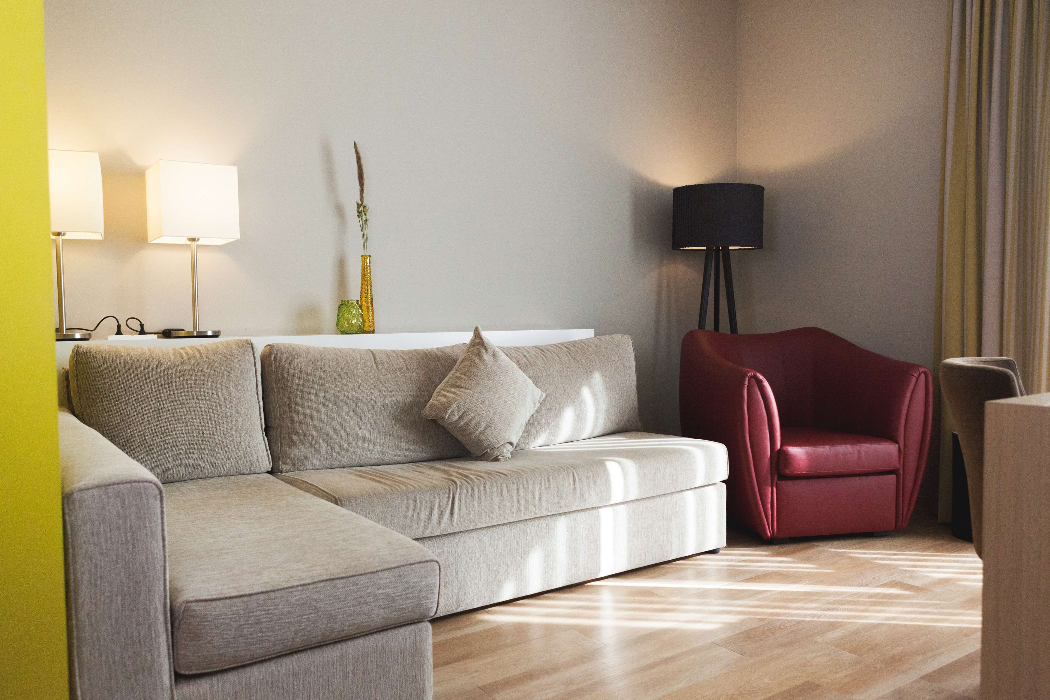 Ein modernes Wohnzimmer mit einem grauen Sofa, einem roten Sessel und zwei Stehlampen.