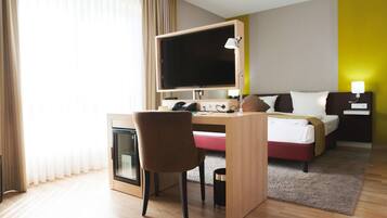 Een hotelkamer met een bed, bureau, stoel, televisie, nachtkastje, lamp en een kleine prullenbak.