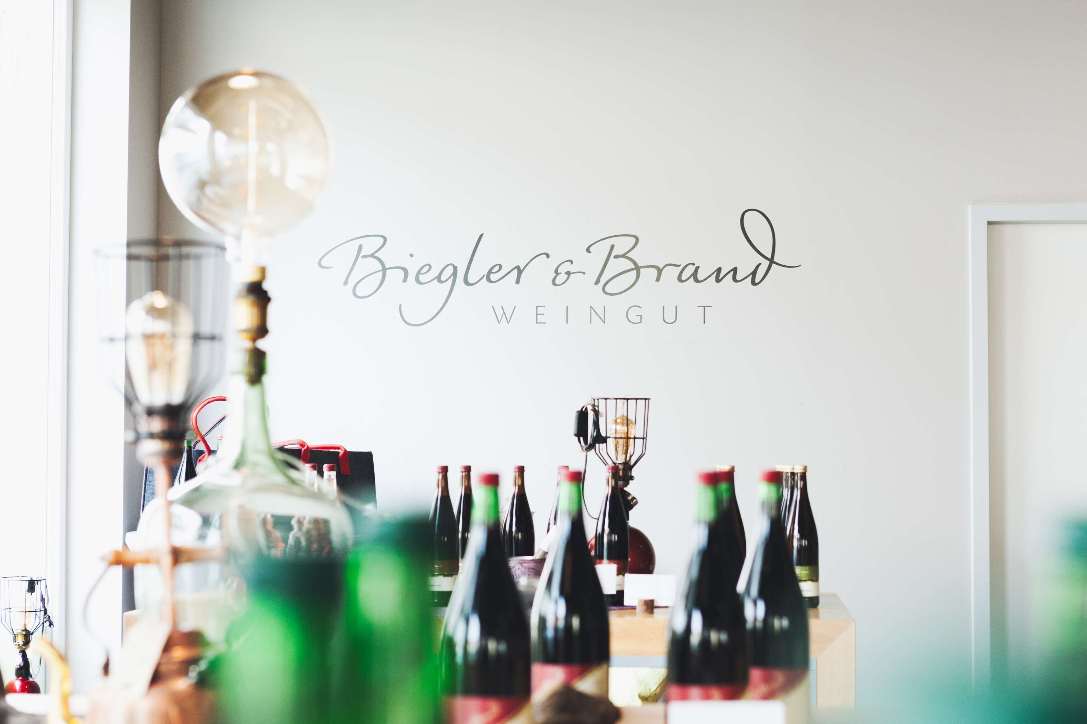 Una habitación con una pared que muestra 'Biegler & Brand WEINGUT' y varias botellas de vino sobre una mesa.