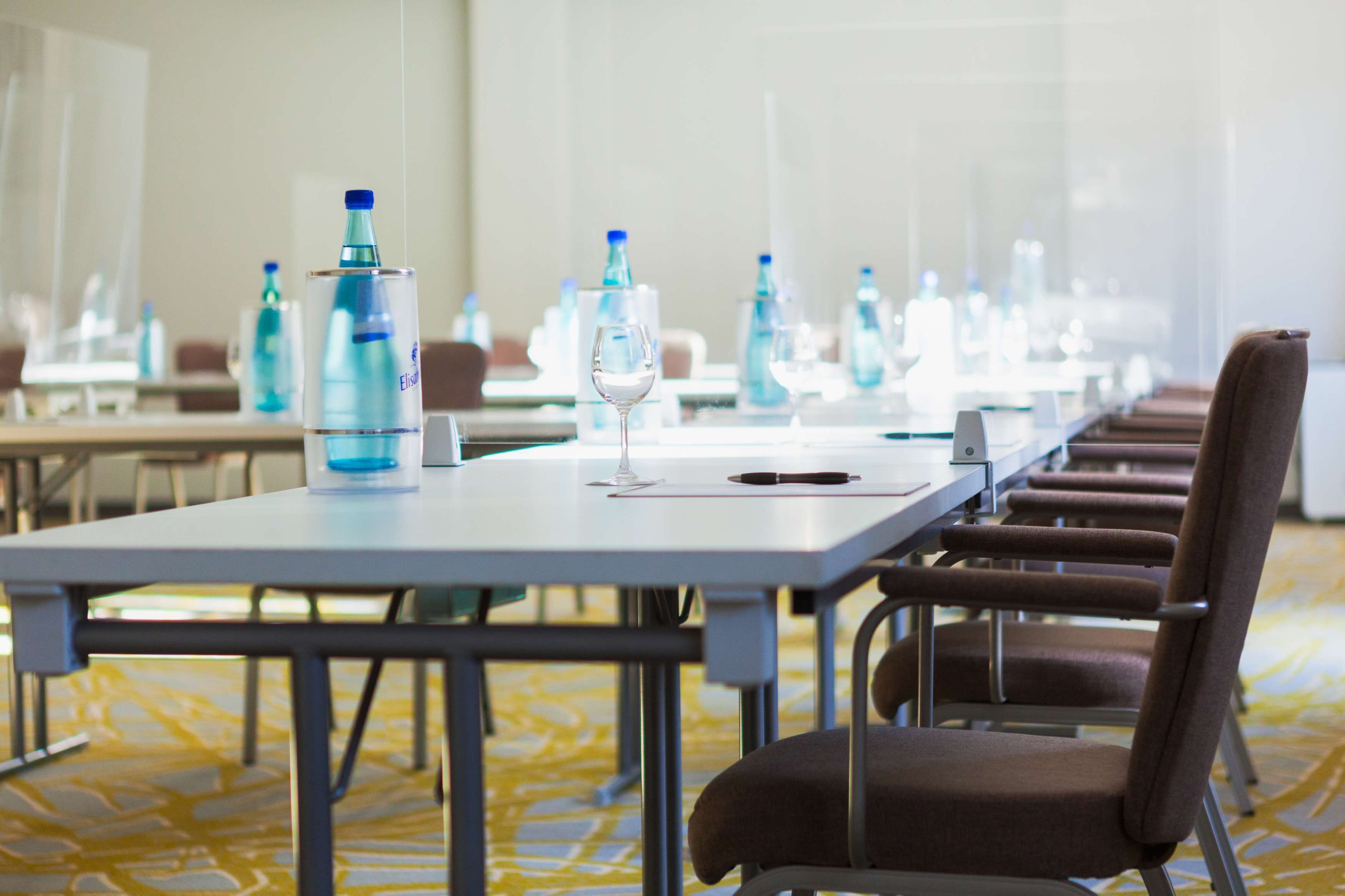 Un salón de conferencias con mesas, sillas, botellas de agua y una copa de vino.