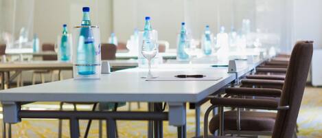 Un salón de conferencias con mesas, sillas, botellas de agua y una copa de vino.