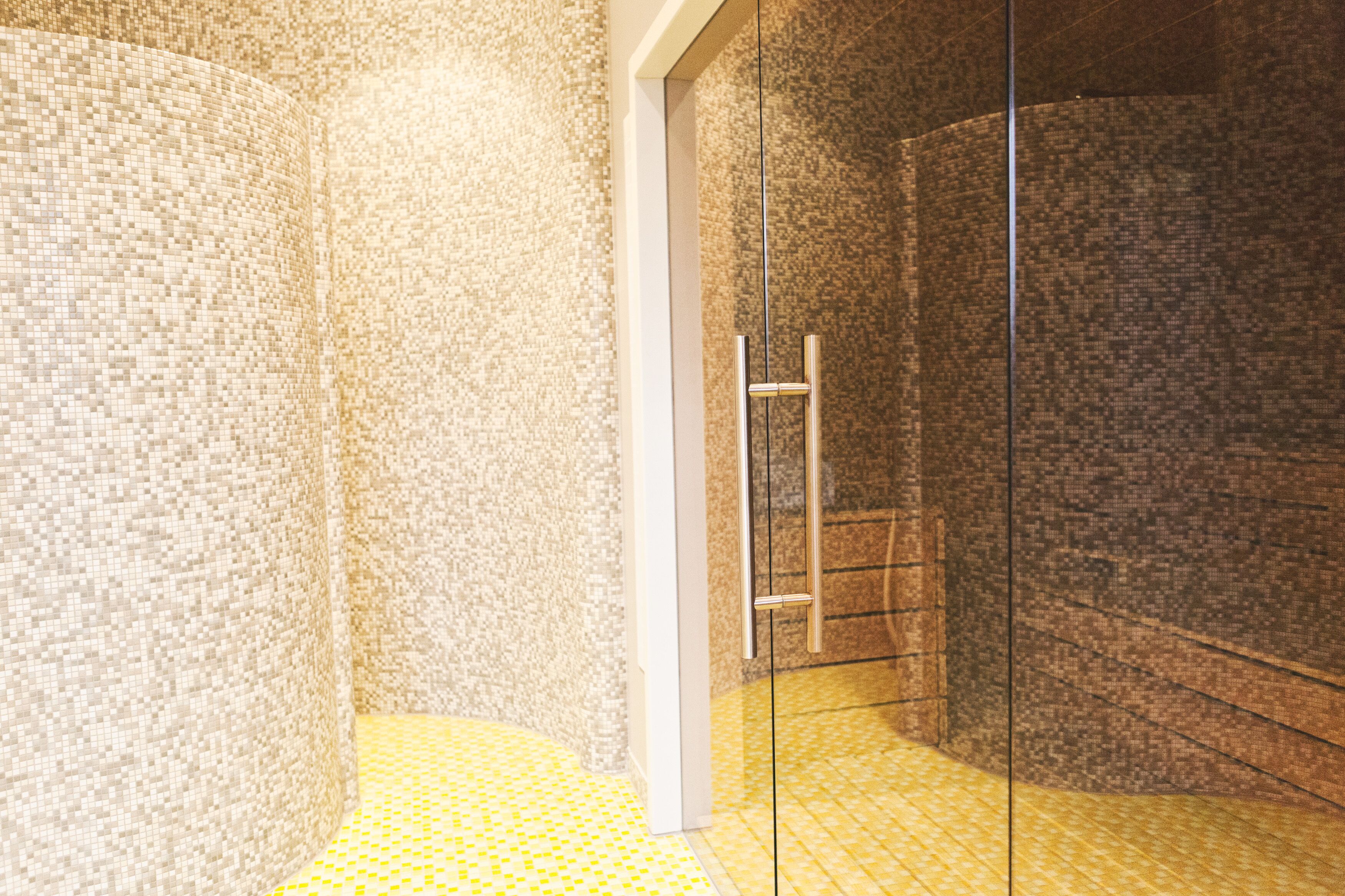 Área de chuveiro com paredes e chão revestidos de azulejos, uma escada de metal e um batente de porta branco.