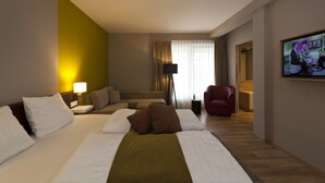 Habitación de hotel con una cama grande, un sofá, un sillón rojo, un televisor y una lámpara de pie.