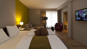 Habitación de hotel con una cama grande, un sofá, un sillón rojo, un televisor y una lámpara de pie.