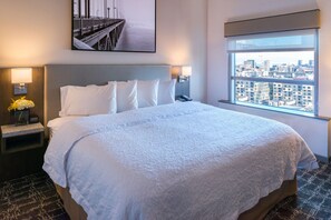 A hotel room with a large bed, a nightstand with a lamp, and a window with a city view. - Hampton Inn San Francisco Downtown/Convention Center (San Francisco)