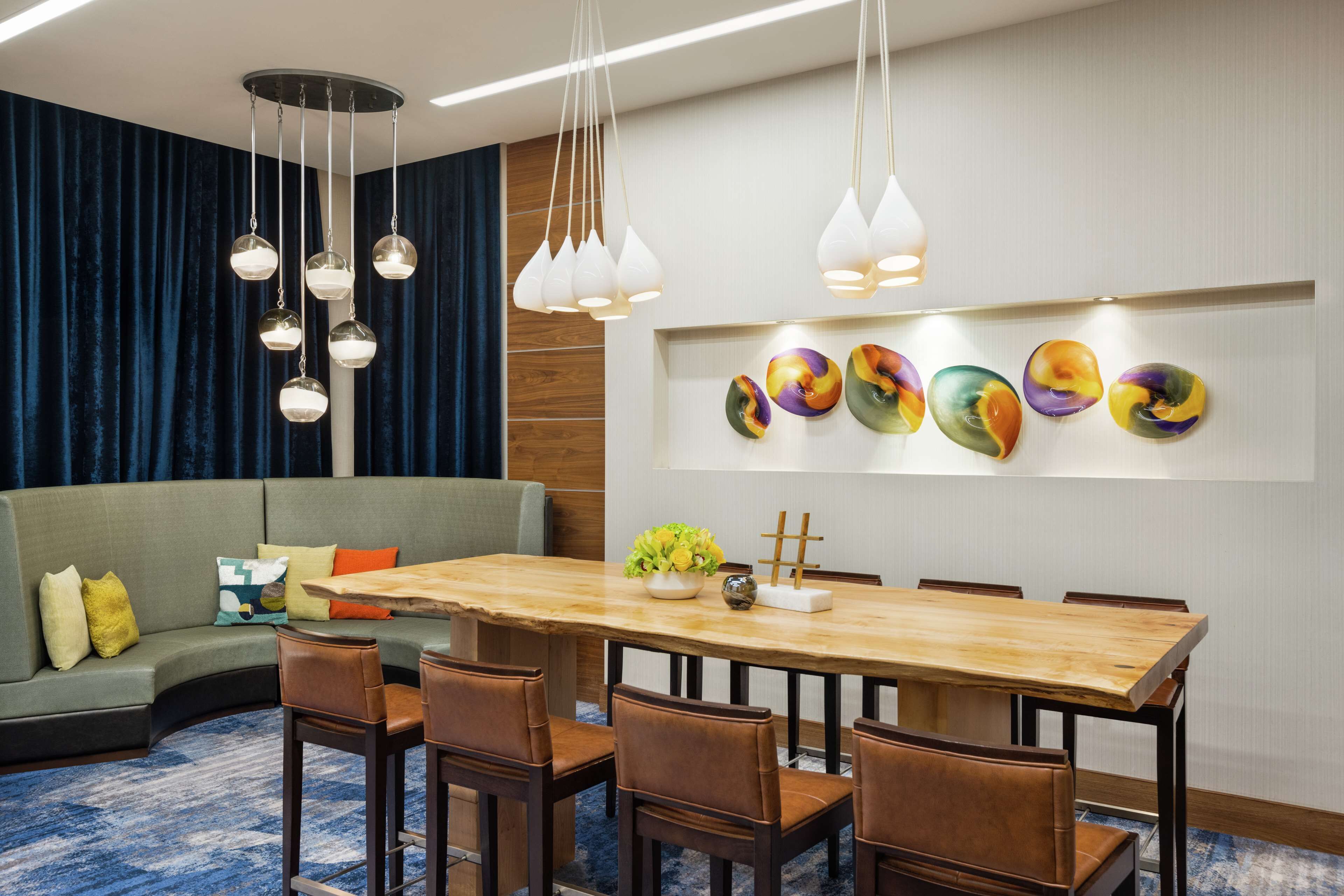 A modern dining area with a wooden table and brown chairs, a blue carpet, and a blue curtain backdrop.