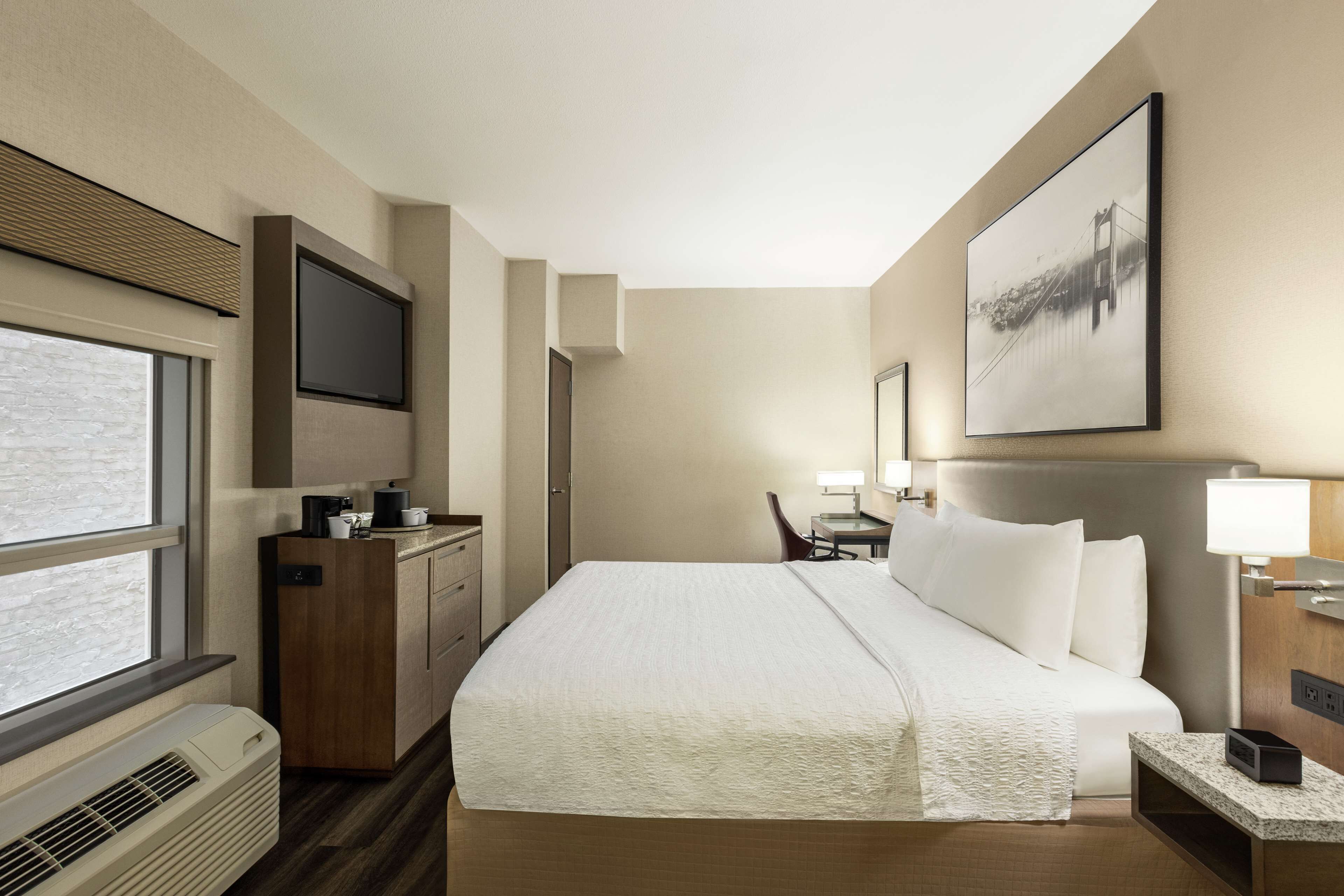 A hotel room with a large bed, a desk, a chair, a TV, and a window.