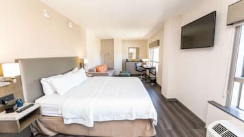 A hotel room with a large bed, bedside table, lamp, and a TV mounted on the wall.