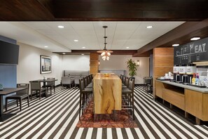 A modern dining area with a central wooden table, surrounded by chairs, and a counter with coffee machines. - Hampton Inn San Francisco Downtown/Convention Center (San Francisco)