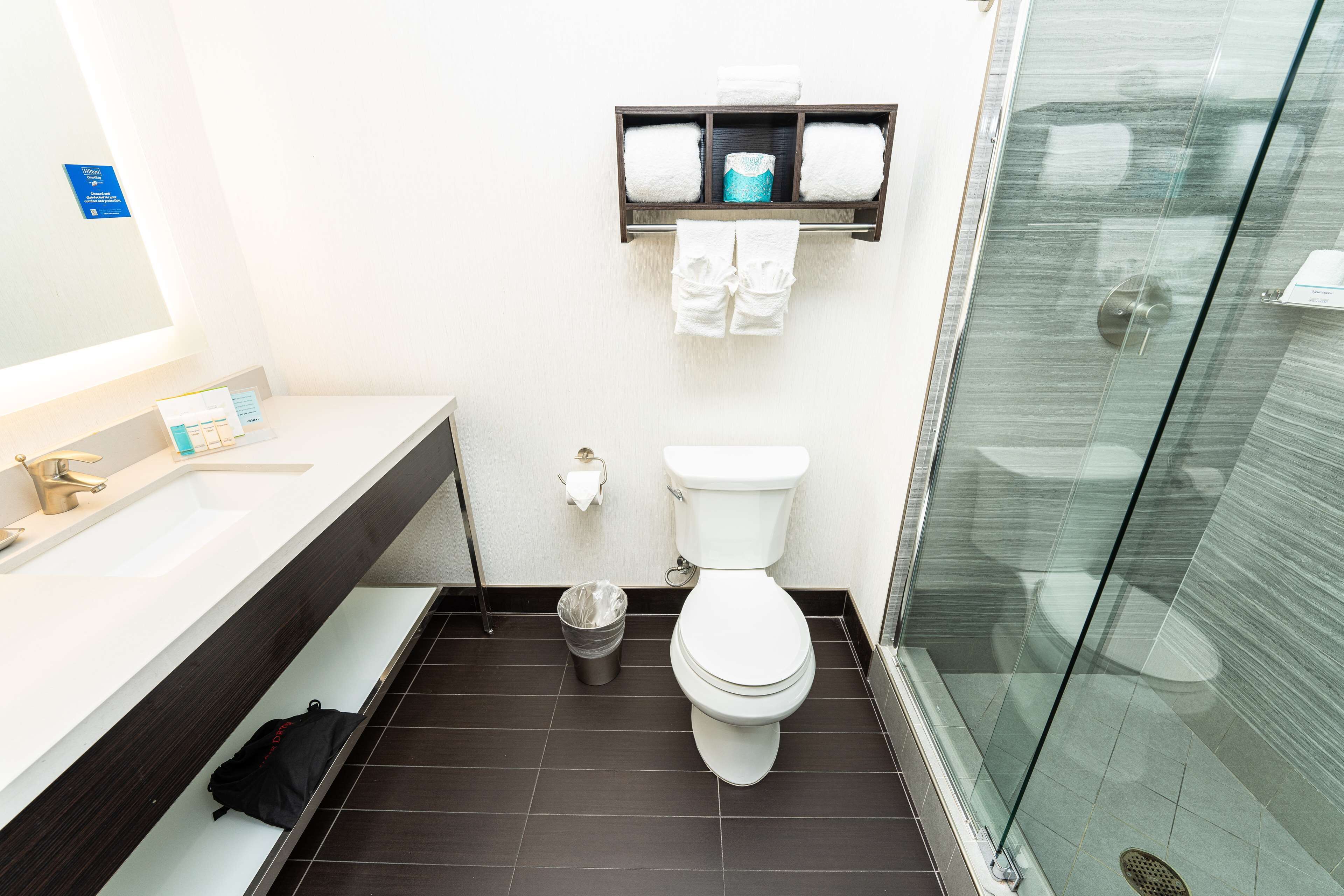 Une salle de bain moderne avec une douche à parois de verre, des toilettes blanches et une poubelle noire.
