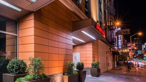 A modern building with a warm-toned facade, large planters with greenery, and a well-lit entrance. - Hampton Inn San Francisco Downtown/Convention Center (San Francisco)