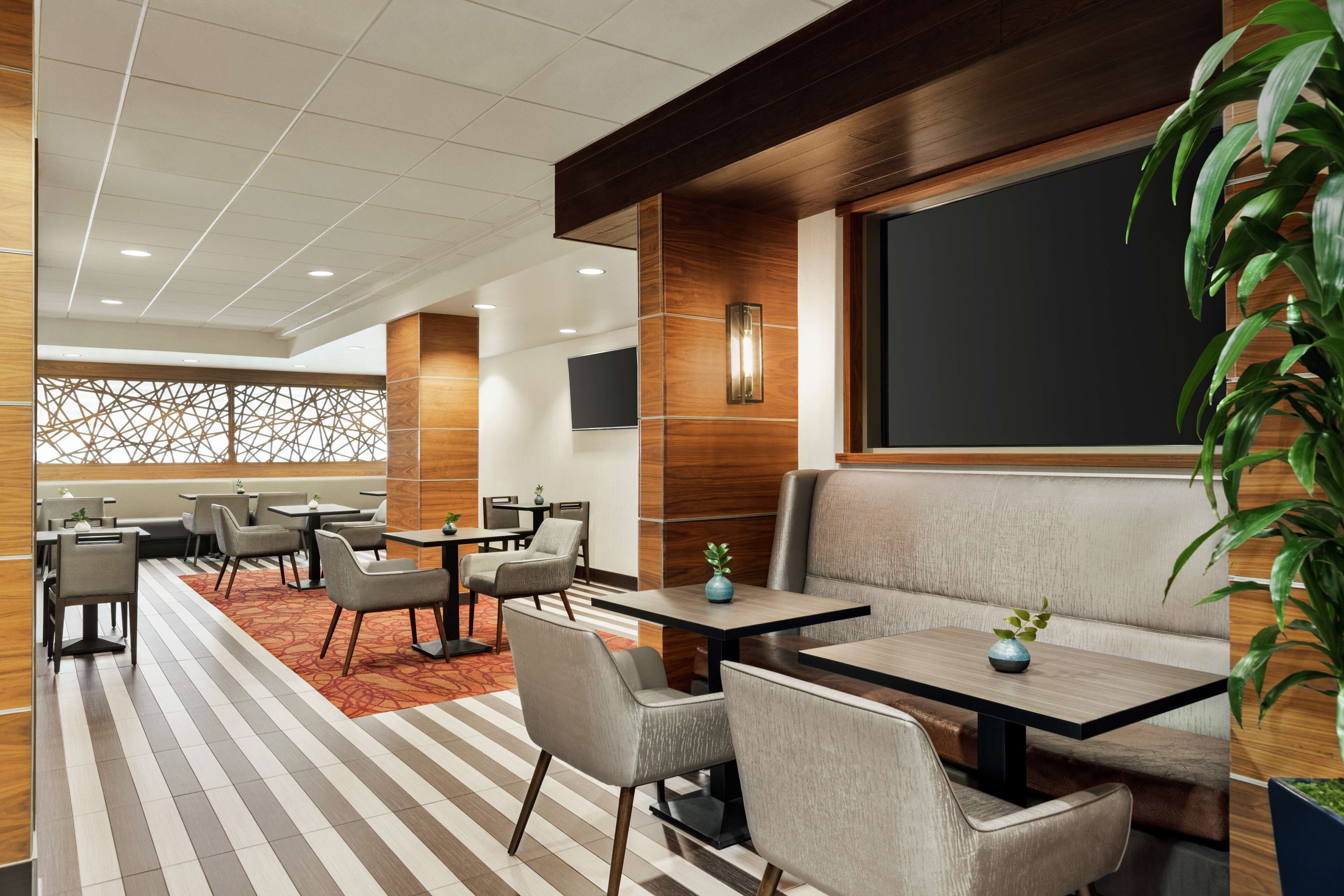 A modern hotel lobby with a seating area, tables, and a large screen.