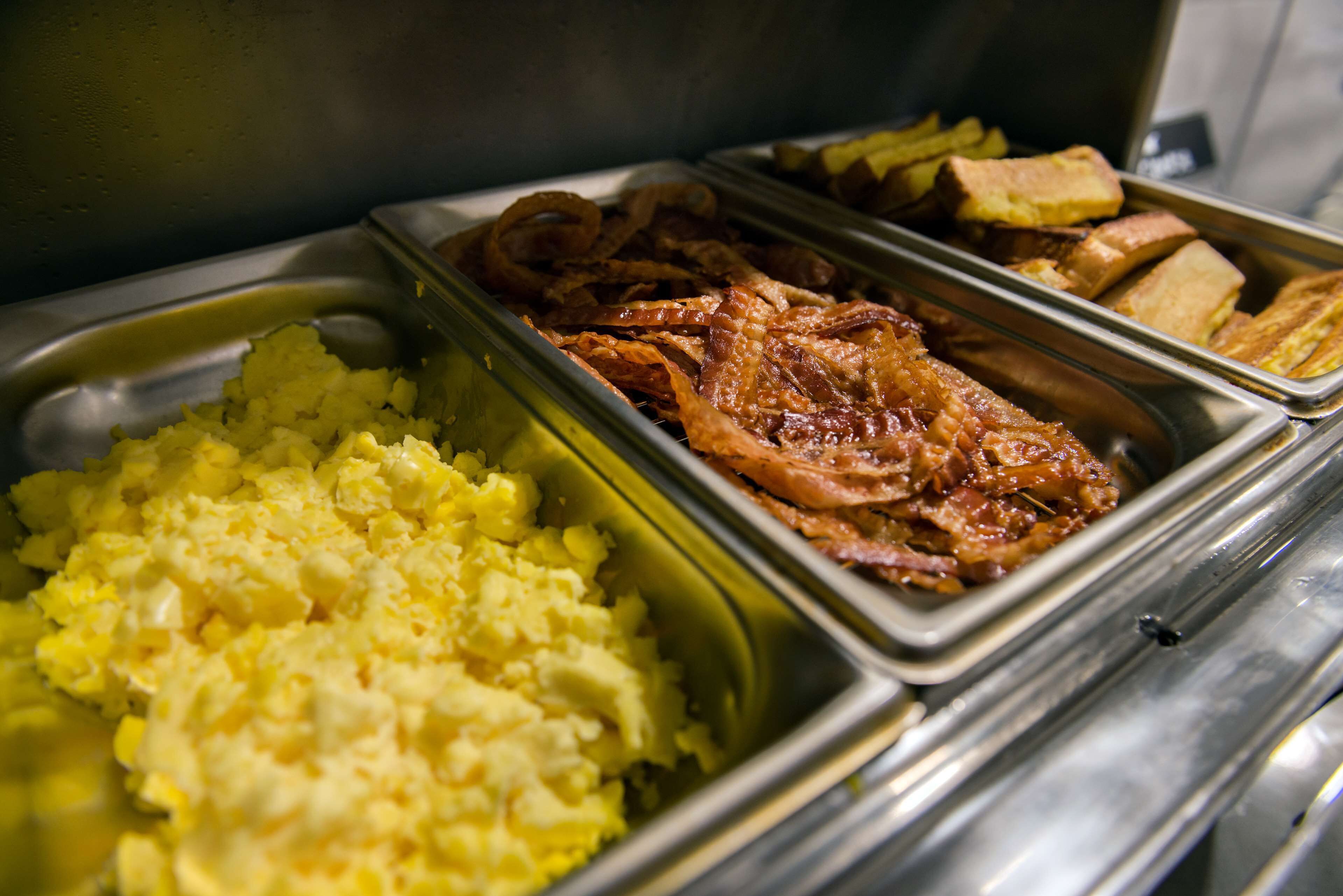 A buffet with scrambled eggs, bacon, French toast, and hash browns.