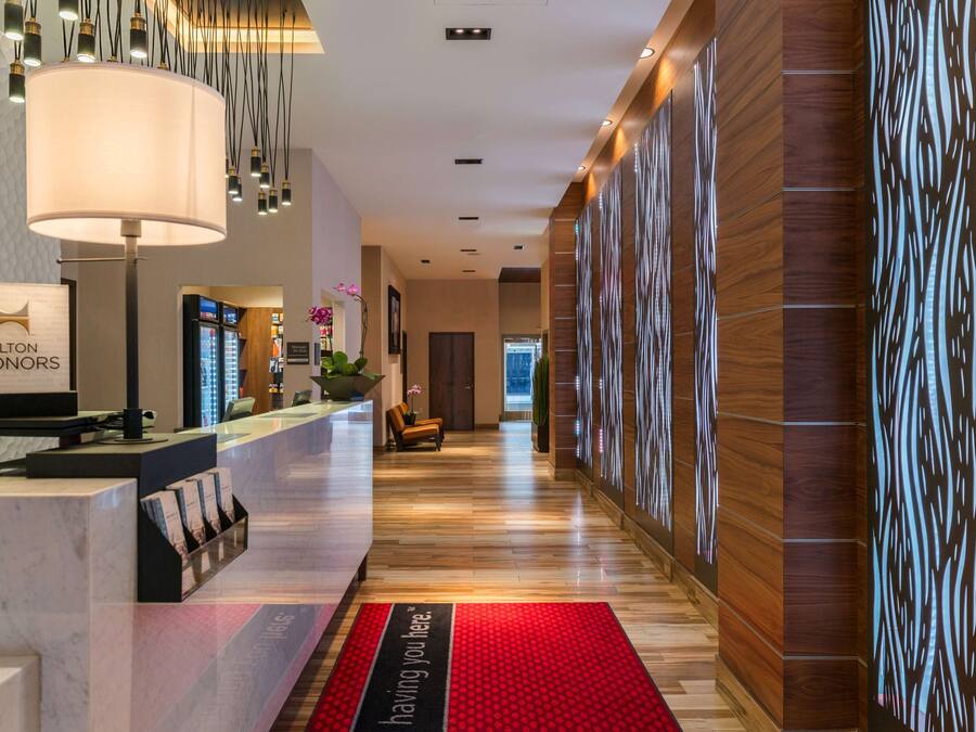Ein Hotel-Rezeptionsbereich mit einer Marmor-Theke, einer großen Lampe und einem roten Teppich mit Aufdruck.