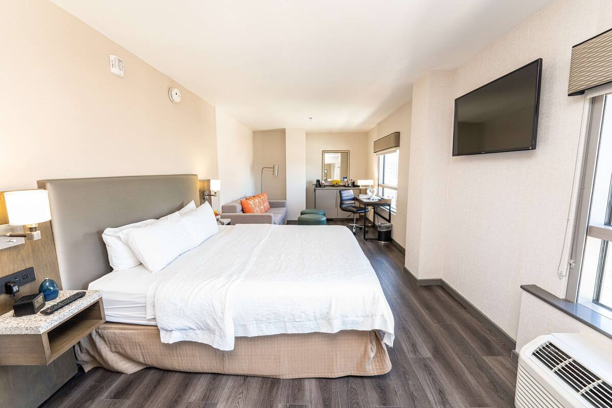 A hotel room with a large bed, a desk, a chair, a TV, and a window.