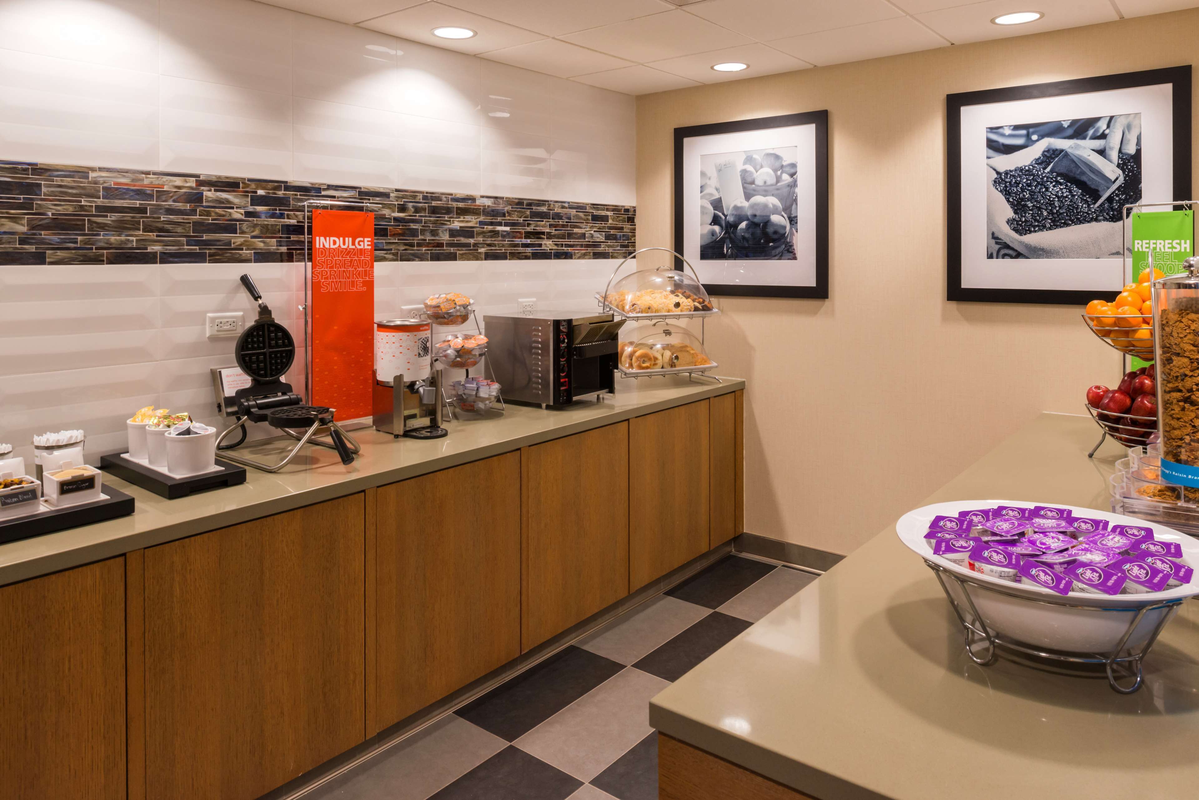 Zona de recepción de un hotel con diseño moderno, que incluye un mostrador de registro, una estación de café y un frutero.