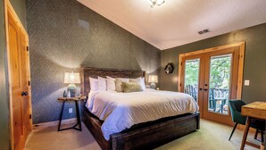 A bedroom with a large bed, a wooden headboard, a small table with a lamp, and a view through a door to an outdoor area. - Engen Hus Bed and Breakfast (Salt Lake City)