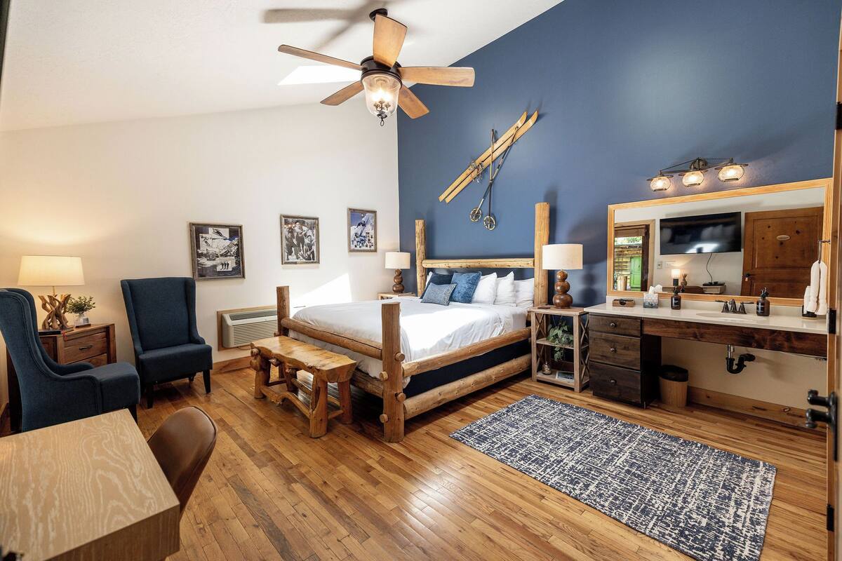 A bedroom with a wooden bed, a desk, a chair, a ceiling fan, and a large mirror.