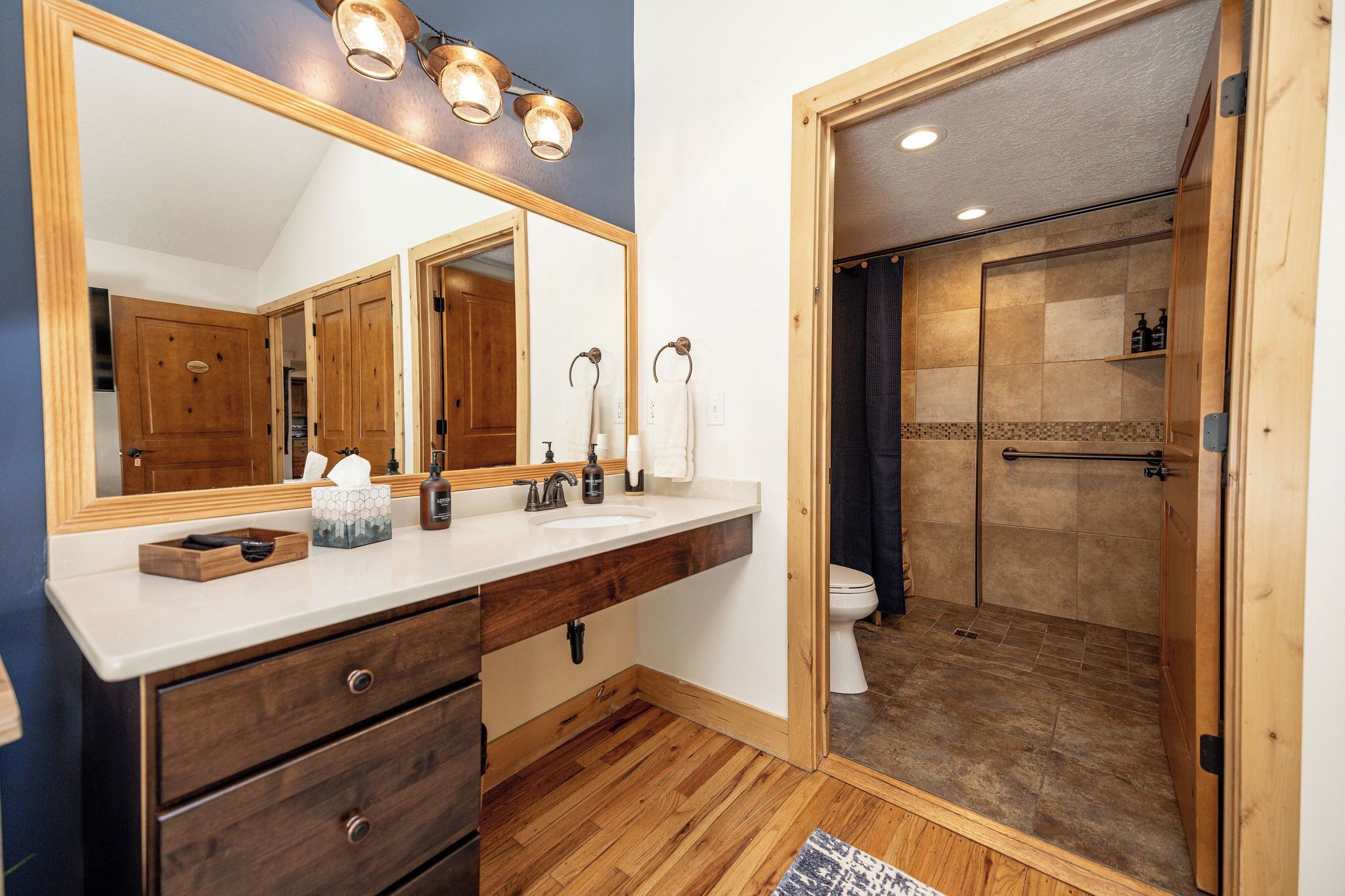 A bathroom with a wooden vanity, a large mirror, and a shower area.