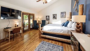 A bedroom with a wooden bed, a desk, and a chair. There is a ceiling fan, a TV, and a window with a view of the outdoors. - Engen Hus Bed and Breakfast (Salt Lake City)