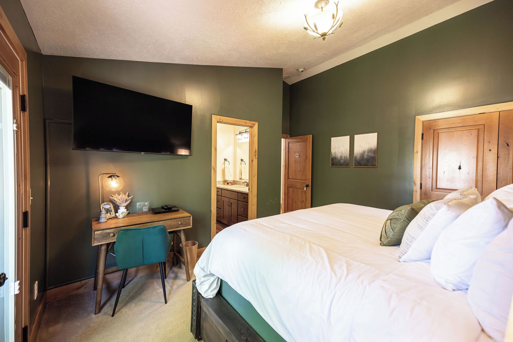 A bedroom with a bed, a desk with a chair, a television, a mirror, and a wardrobe.