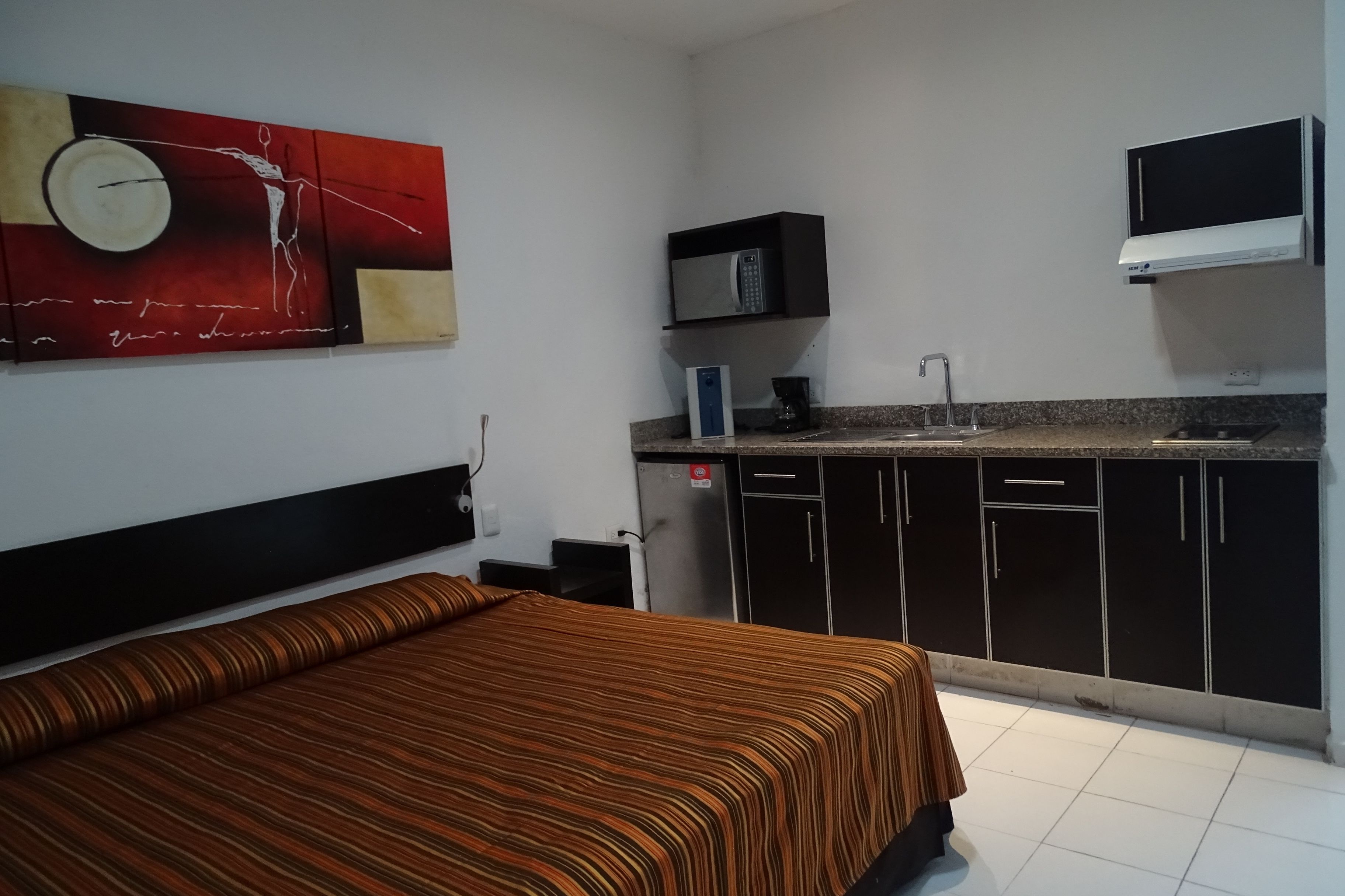 A hotel room with a bed, a kitchenette with a microwave, and a TV.