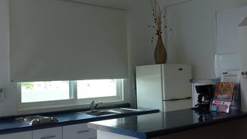Cozinha com armários brancos, bancada preta, geladeira branca, máquina de café e um vaso com galhos no balcão.