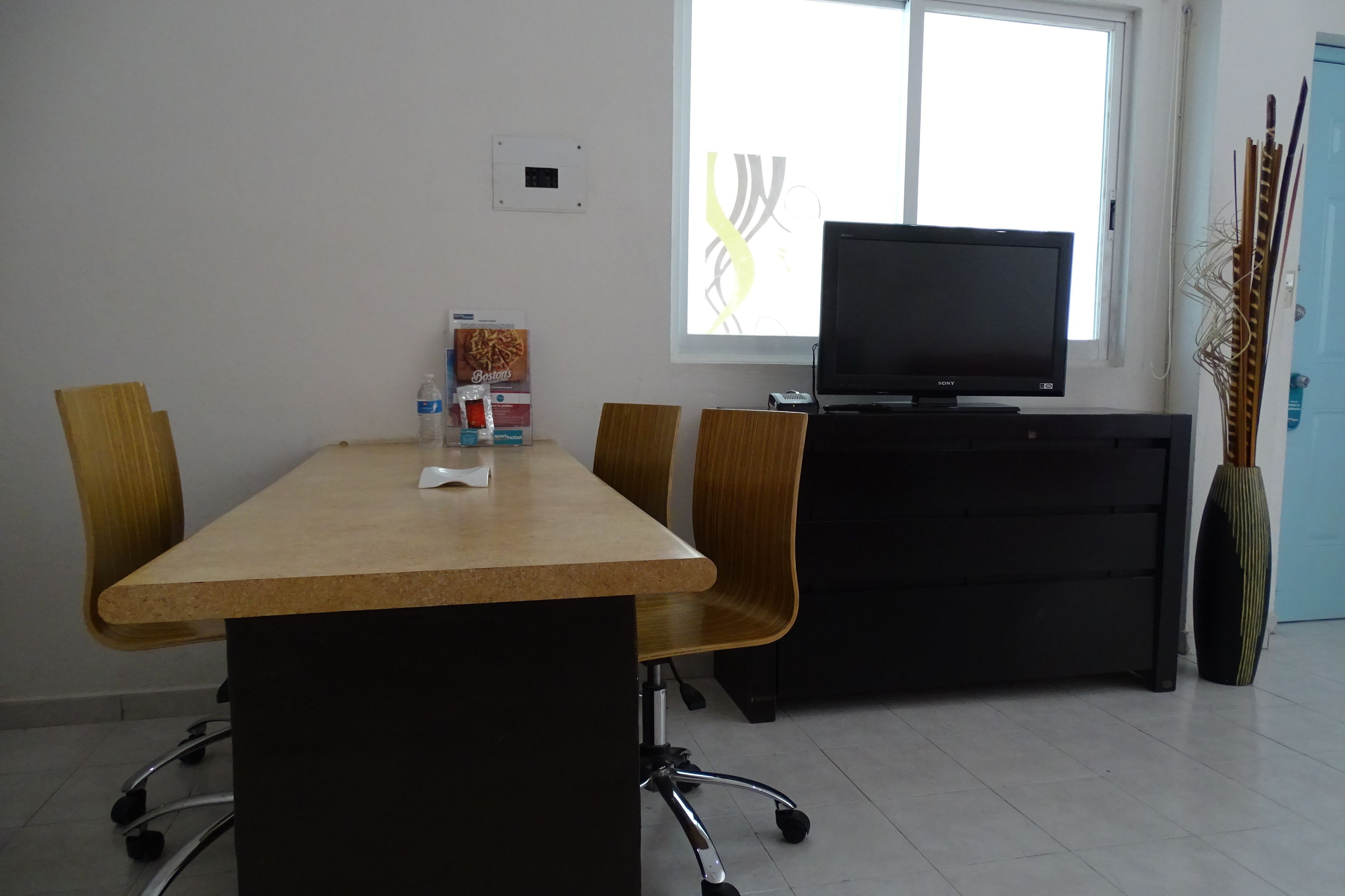 Un salón de conferencias con una larga mesa, cuatro sillas, un televisor sobre un soporte, una botella de agua y un paquete de comida.