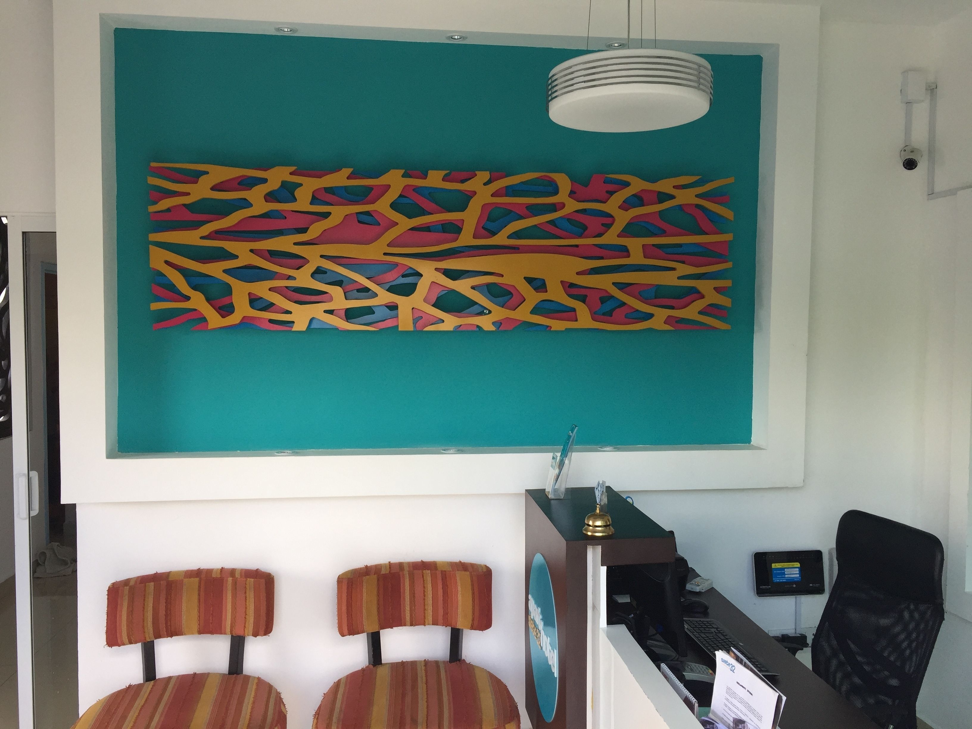 A reception area with a teal-colored abstract wall art, two striped chairs, a desk with a computer, and a security camera.