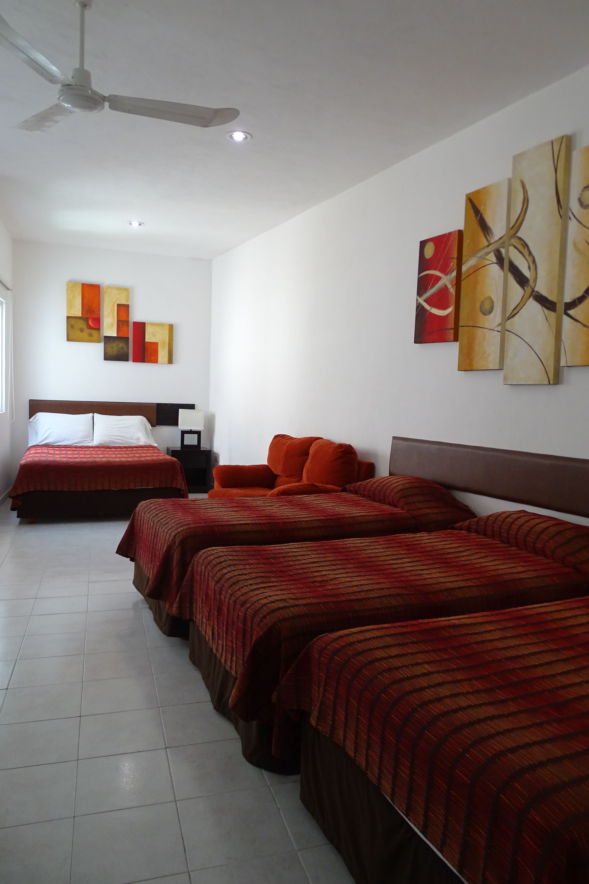 Una habitación de hotel con dos camas, un ventilador de techo y arte abstracto en las paredes.