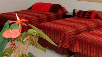 A room with two beds, a red and black striped bedspread, a red pillow, and a single orange chair.