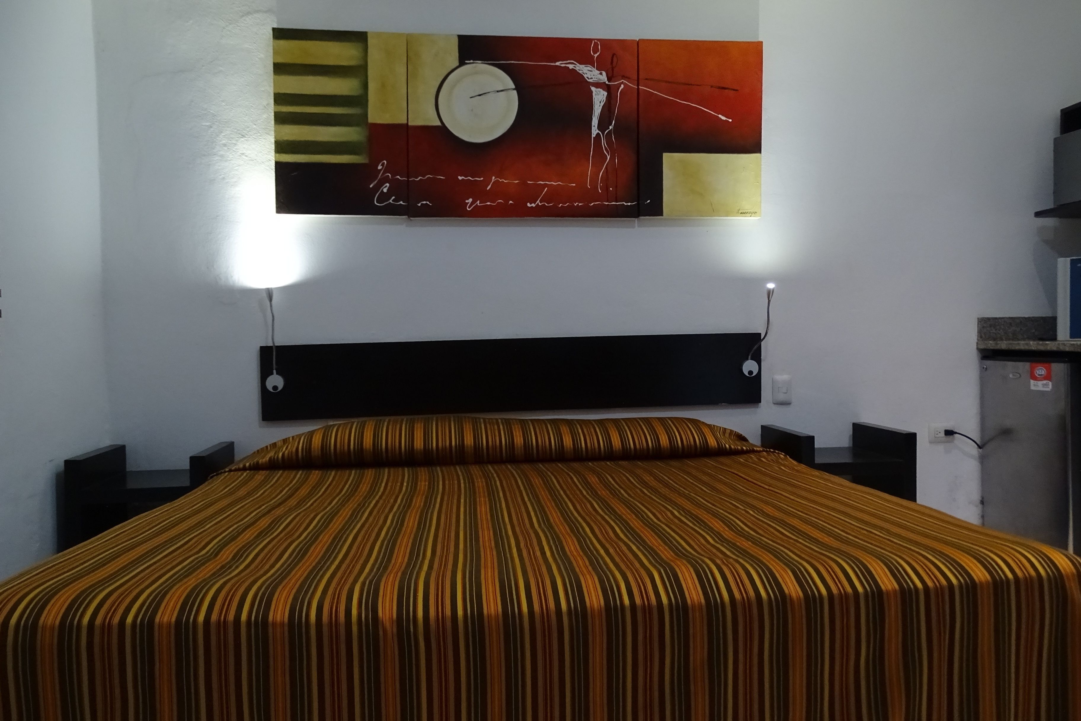 A hotel room with a bed, a wall clock, and a painting.