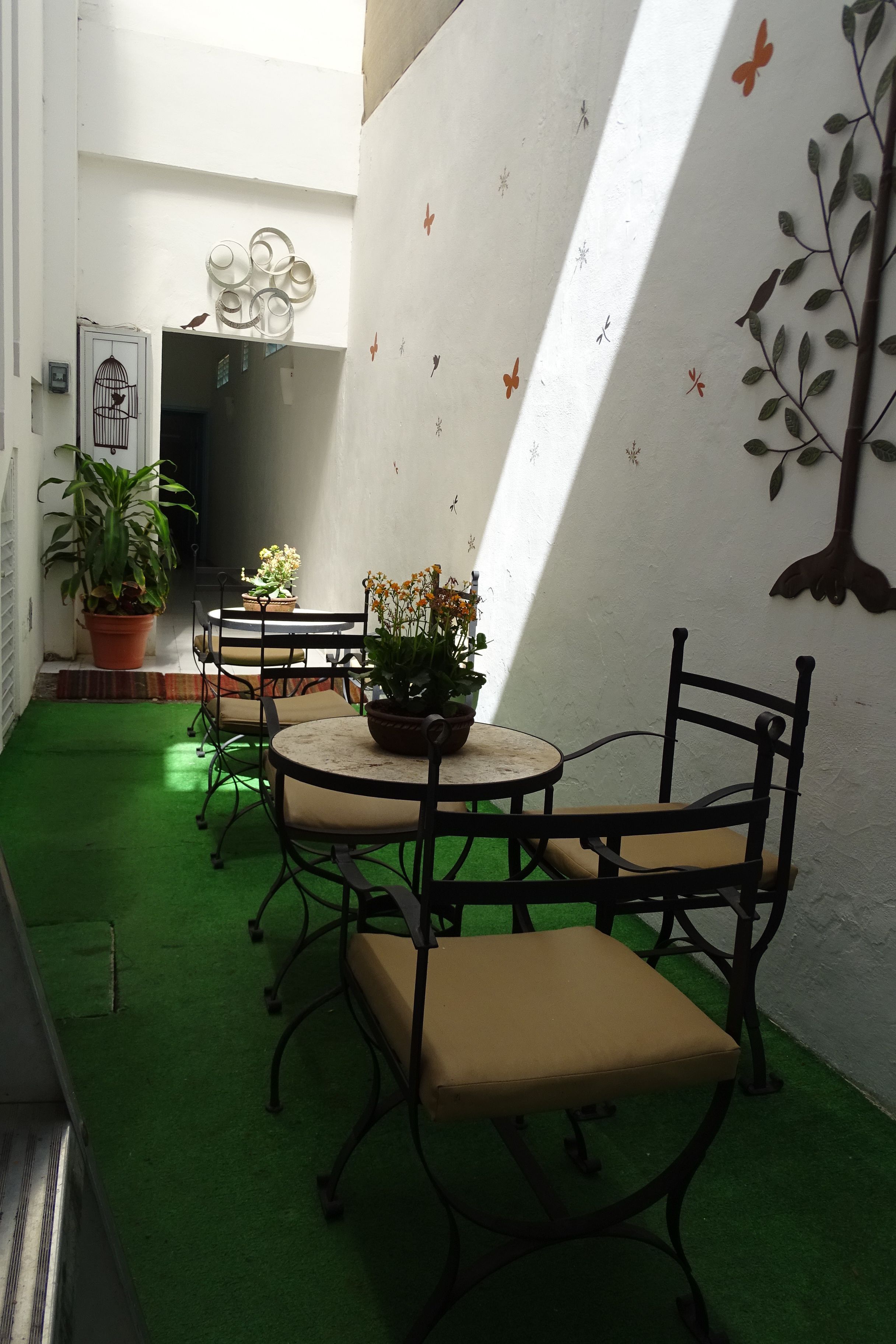 A small, enclosed patio area with a round table and chairs, surrounded by potted plants and a decorative wall.