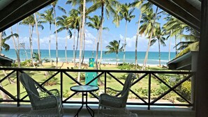 Un balcon avec deux fauteuils en osier et une petite table, donnant sur une plage bordée de palmiers et sur l’océan.
