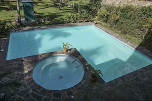 A rectangular swimming pool with a circular hot tub in the center, surrounded by stone tiles and potted plants. - Habitaciones Playa Coson (Las Terrenas)