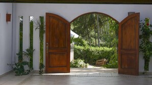 Une porte à deux battants en bois, surmontée d’une arche en demi-cercle, qui donne sur un jardin.