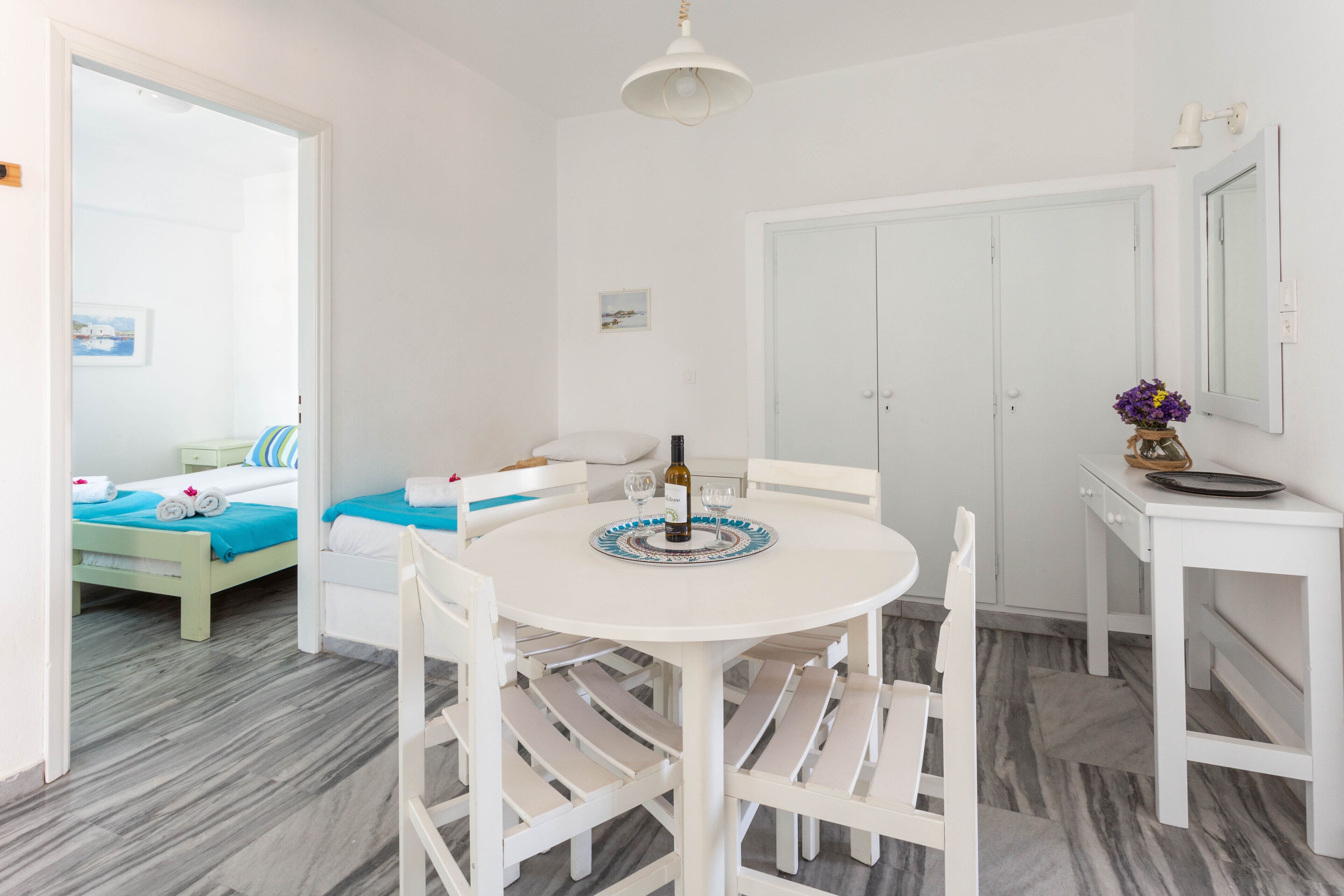 A room with a bed, a dining table with chairs, a small table with a bottle and glasses, and a mirror on the wall.