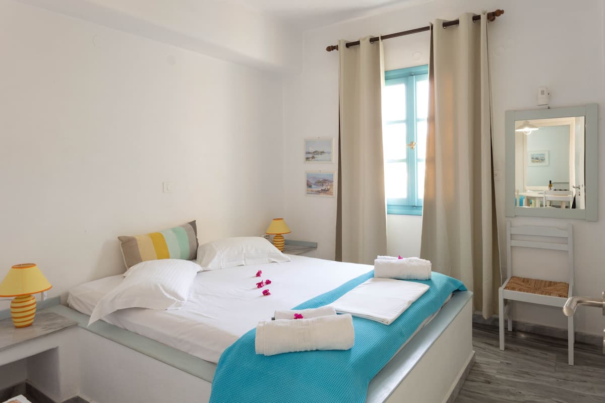 A hotel room with a bed, two bedside tables with lamps, a chair, a mirror, and a window with curtains.