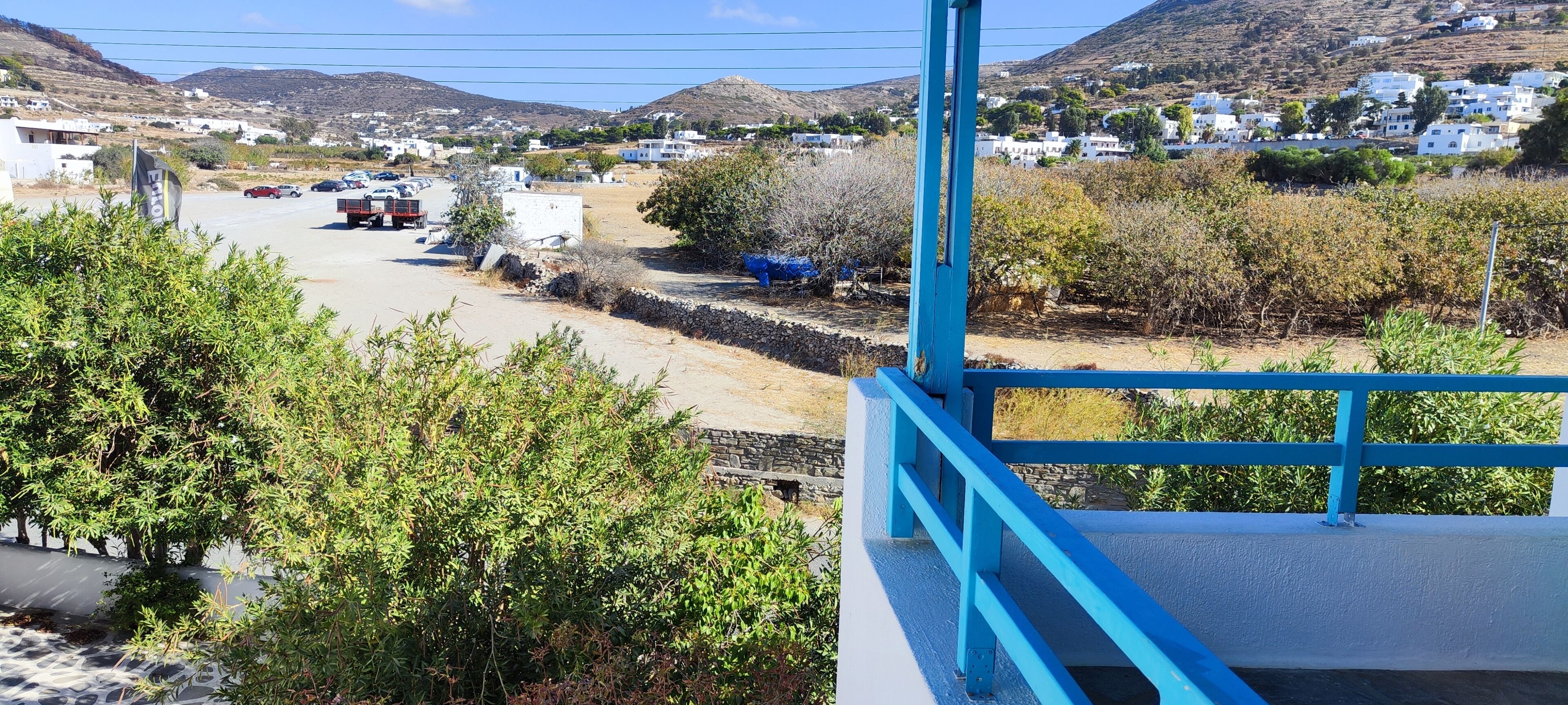 A coastal town with white buildings, a road, and a blue railing.
