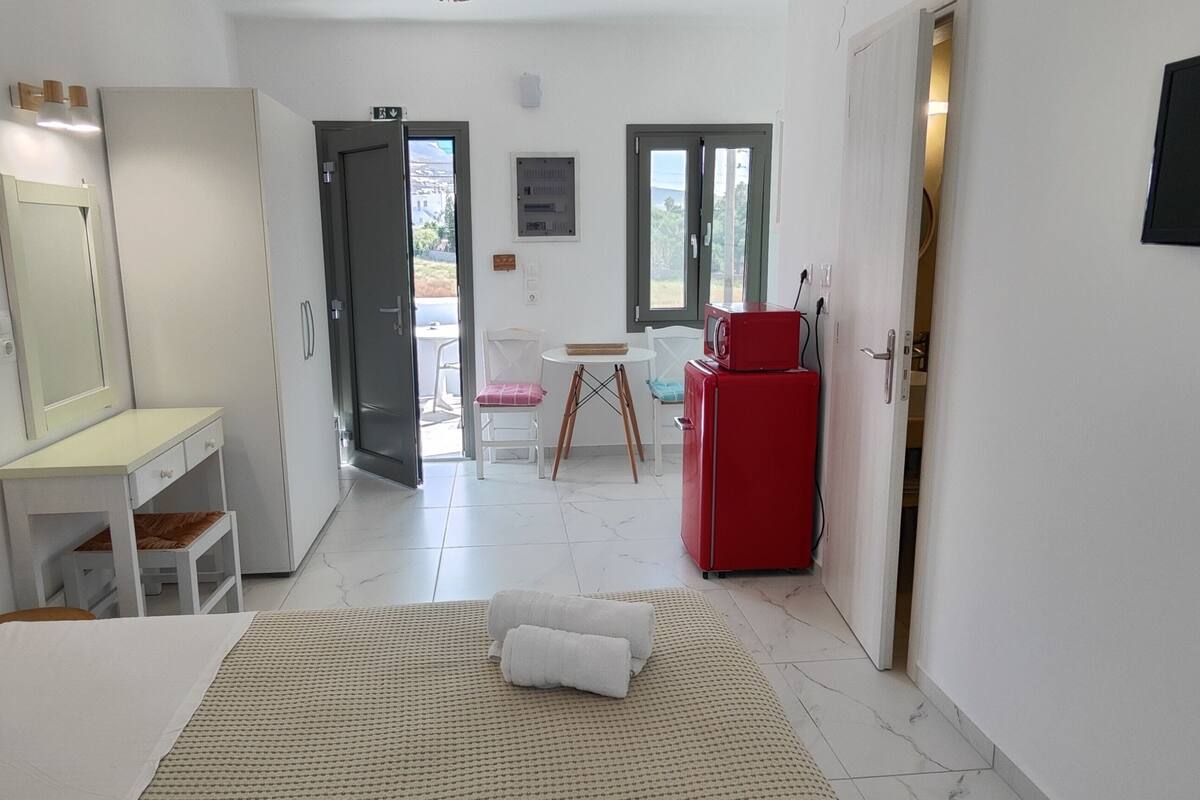 A hotel room with a bed, a desk, a chair, a red refrigerator, and a television.