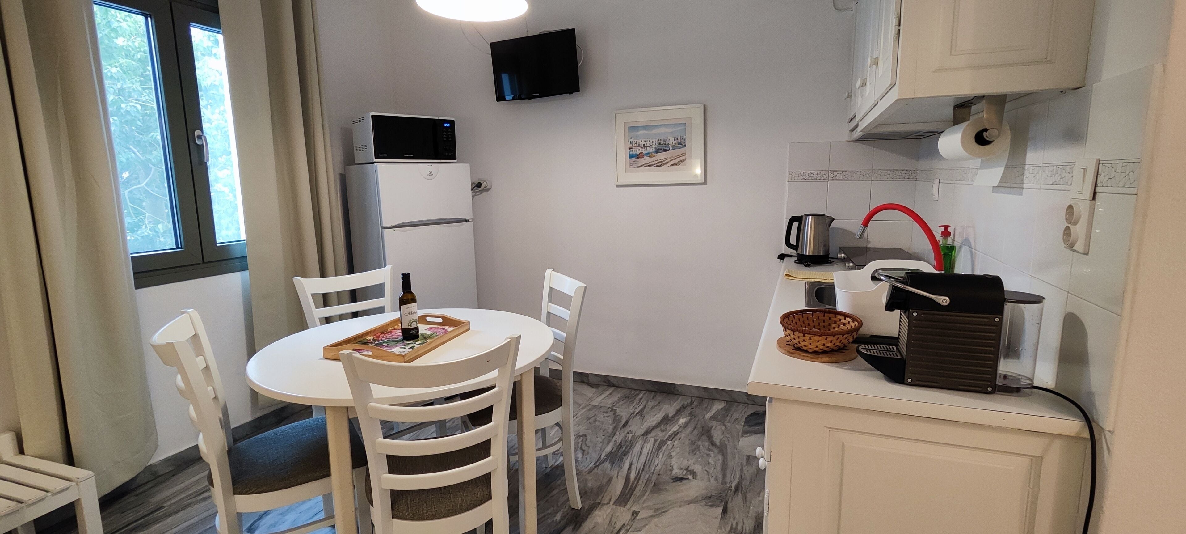 A compact kitchen with white cabinets, a microwave, a refrigerator, and a dining area with white chairs and a table.